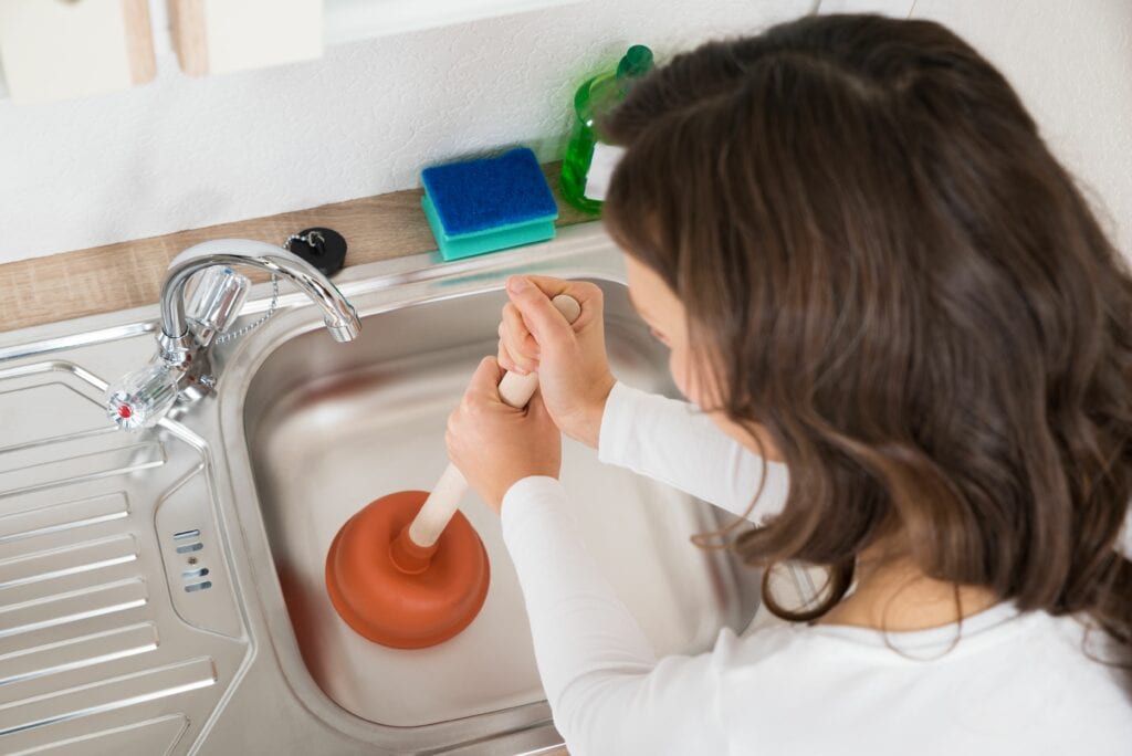 Image of someone trying to unclog their drain with a plunger. Why Do My Drains Keep Clogging?