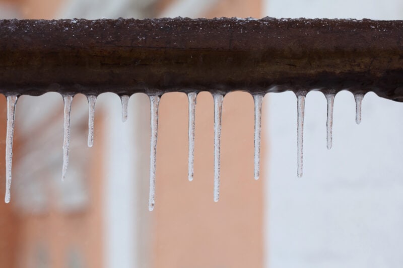 Icicles hanging from a brown pipe. Frozen water and metal surface, winter time concept. selective focus shallow depth of field photo.