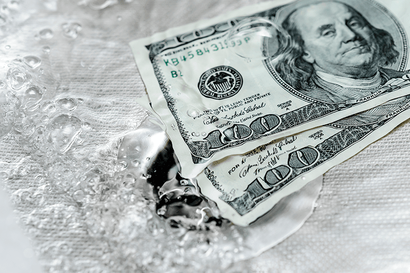 Hundred dollar bills sit in a sink of water. 5 Plumbing Problems Costing You Money.