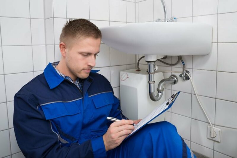 5 Benefits of a Plumbing Maintenance Plan. Image shows Plumbing professional reviewing checklist by sink.
